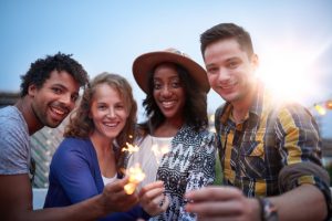 Multi-ethnic millenial group of friendsfolding sparklers on roof